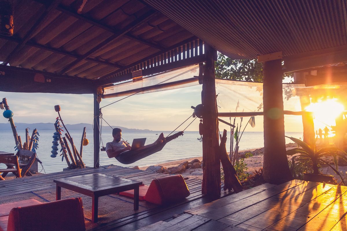 A digital nomad works from a  hammock by the water