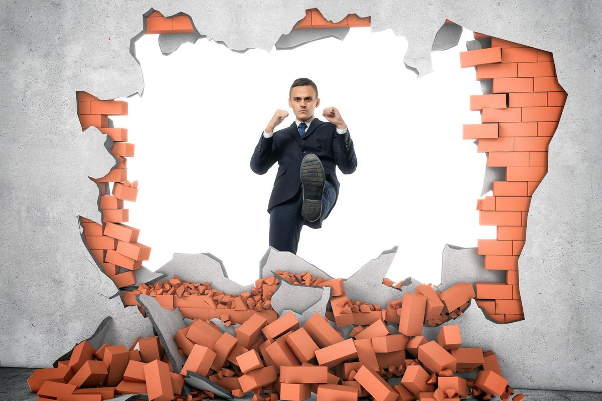 businessman kicks through brick wall
