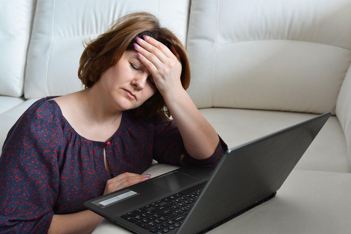 Tired woman with headache uses a computer at home
